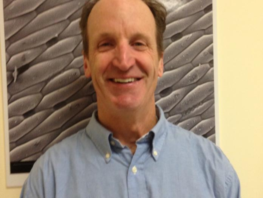 Headshot of a man smiling in front of an Electron Microscopy artwork